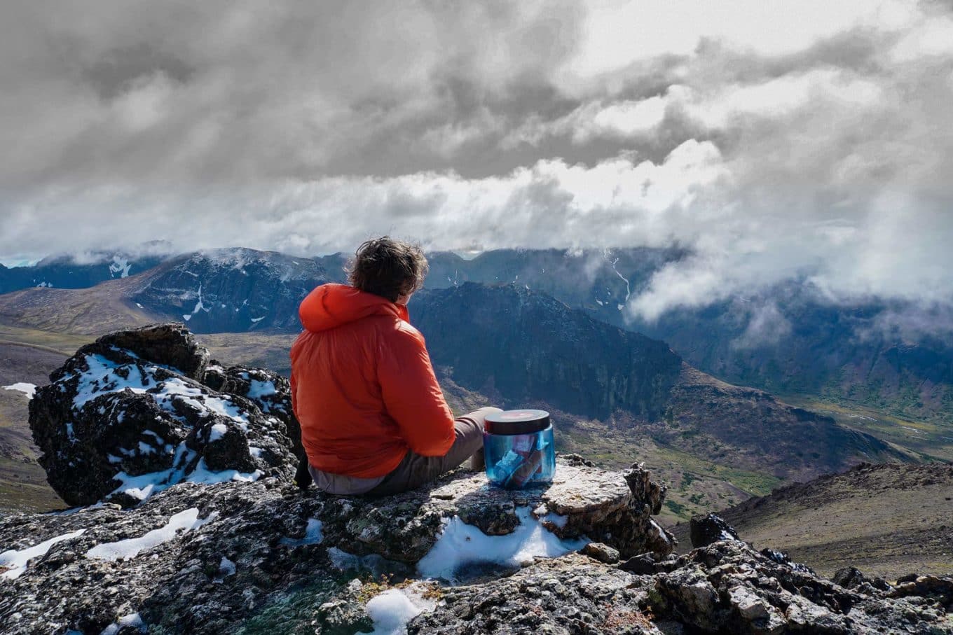 A hiker sitting with a BearVault BV450 Bear Canister in Alaska.
