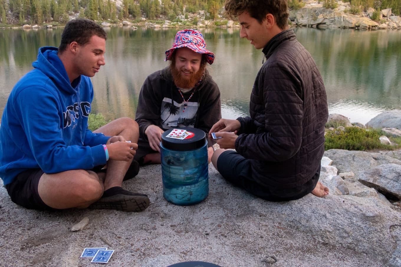 Young men sit on rocky beach and play cards
