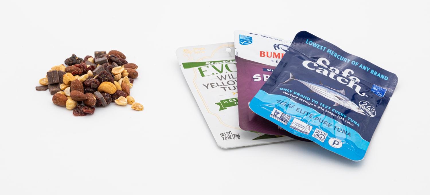 A handful of trail mix next to 3 packets of tuna