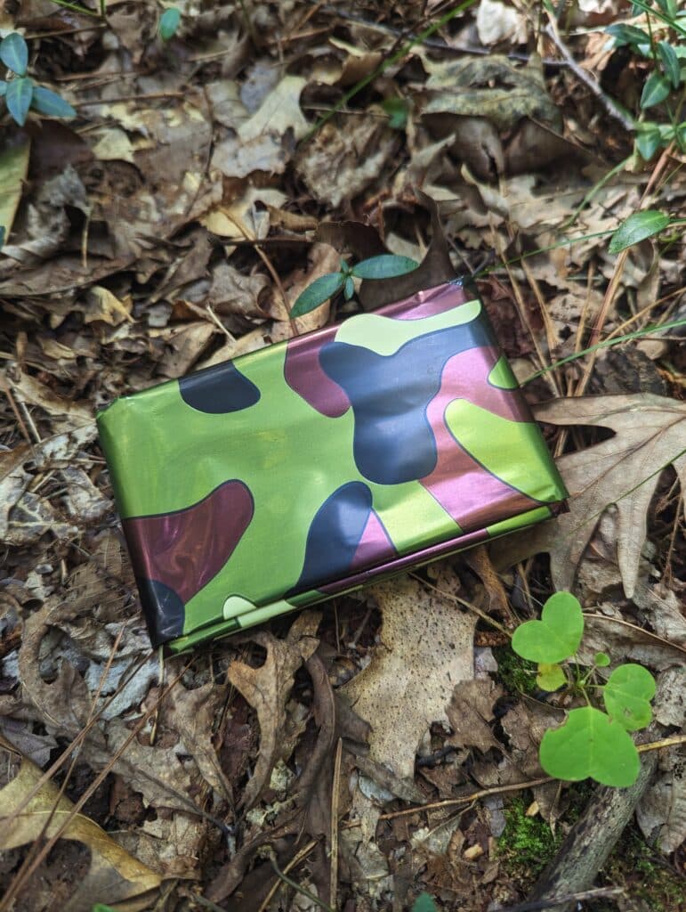 A camouflage emergency space blanket sitting on the ground.