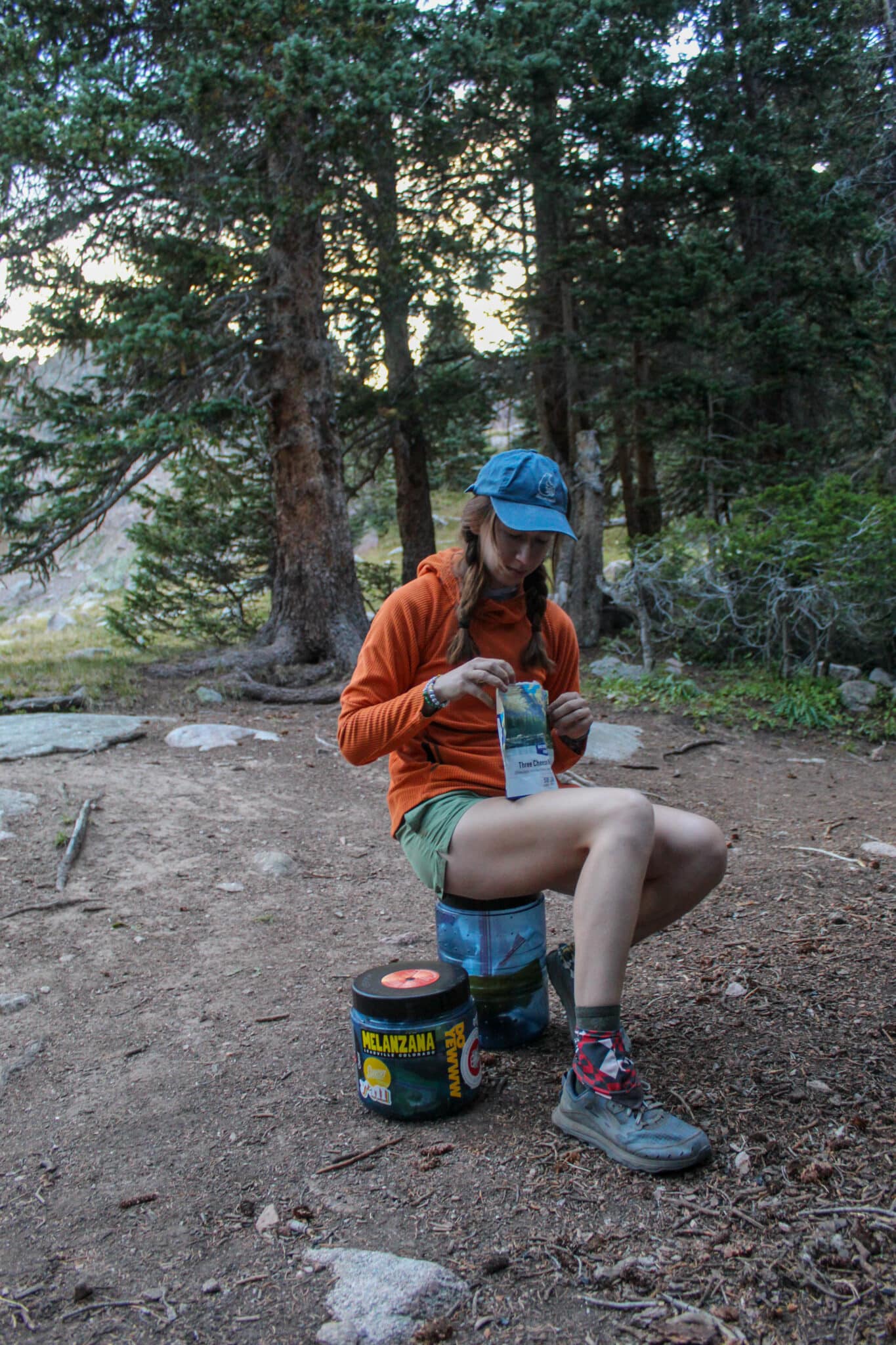 Hiker eating a freeze-dried backpacking meal while sitting on a bear canister.