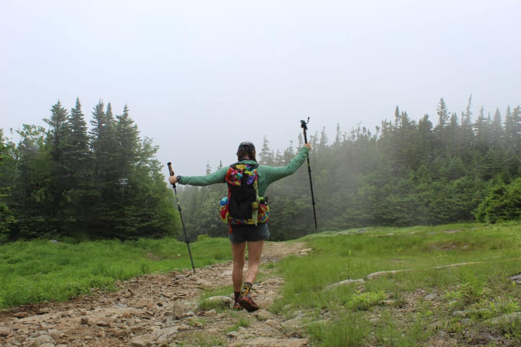 Woman walking down a forested trail right above treeline.