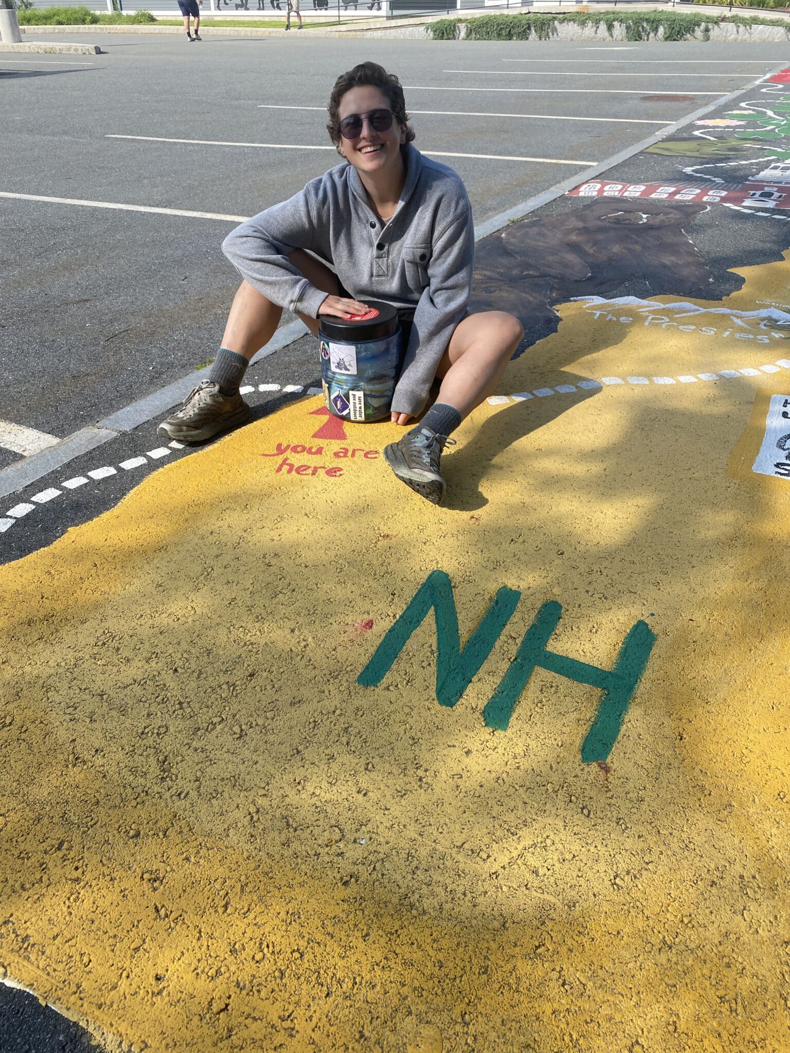 A hiker sits with a bear canister on a piece of chalk art depicting the different states along the Appalachian trail.